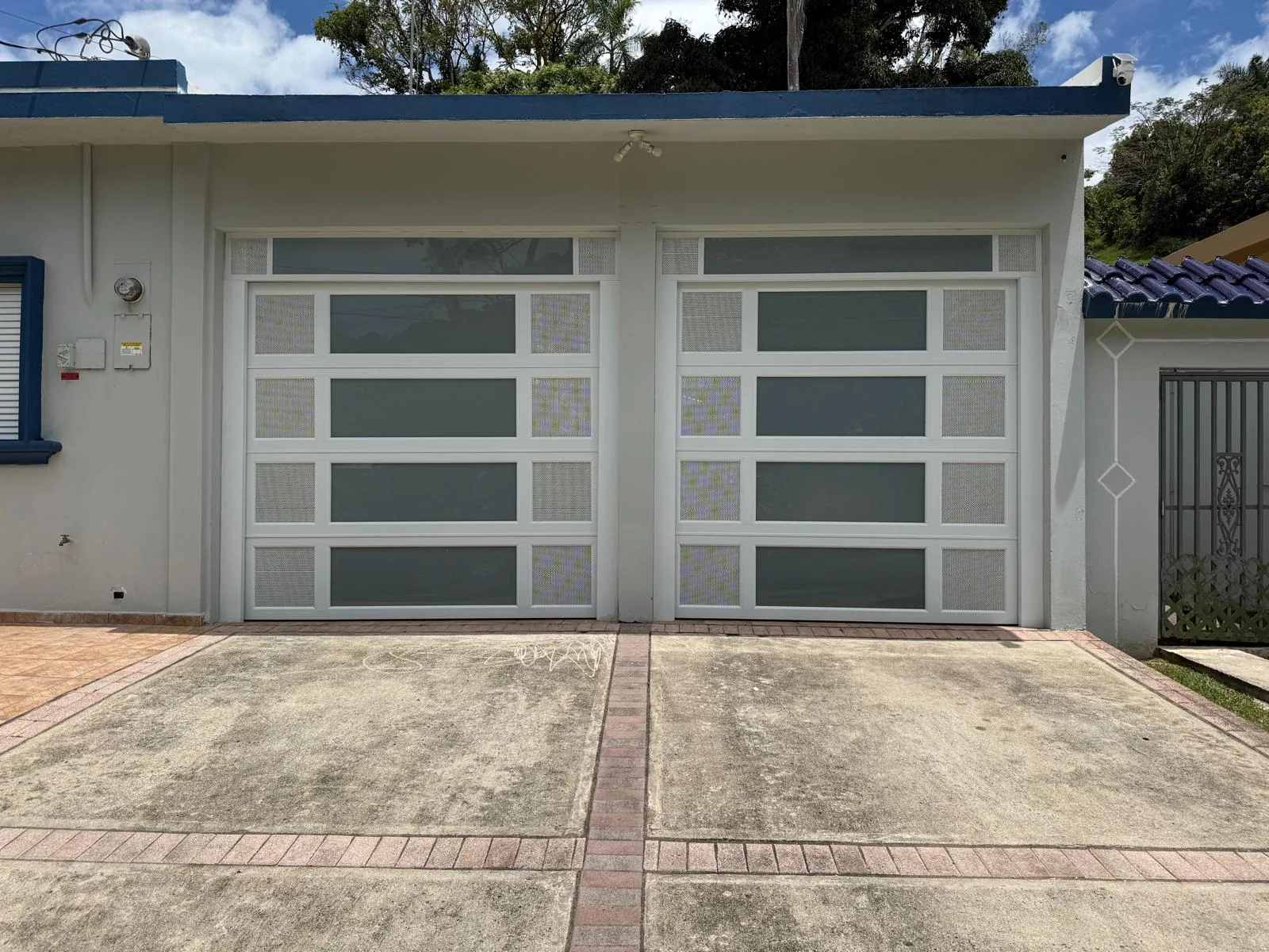 Fachada residencial con dos puertas de garaje blancas con secciones de cristal.